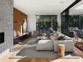 Interior de casa de madera con chimenea de mosaico, sofá modular gris, sillones rosas y acceso a terraza con barbacoa.