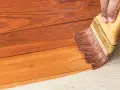 Aplicando barniz a una casa de madera para su mantenimiento. La brocha extiende el producto sobre las tablas.