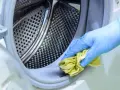 Mano con guante azul limpiando la goma de la lavadora con un paño amarillo. Un método natural para limpiar lavadora vinagre y bicarbonato.