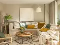Sofá beige con cojines variados, mesa de centro redonda de madera, alfombra estampada y una silla de mimbre. El color topo cual es, se ve en las paredes y cortinas.