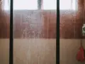 Vidrio de ducha sucio, con marcas de agua y jabón. Un recordatorio visual de cómo limpiar cristales para un baño reluciente.