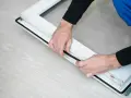 Man installing a black rubber seal on a white window frame, demonstrating como poner burletes en ventanas correderas.