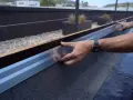 Instalación de tela asfáltica en tejado, un operario ajusta un perfil metálico.