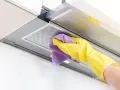 Mano con guante amarillo y paño morado limpiando el interior de la campana extractora, eliminando grasa y suciedad para un hogar reluciente.