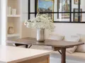 Un jarrón con flores blancas decora la mesa de madera rústica. El espacio alrededor de la mesa comedor es acogedor, con un banco tapizado y cojines.