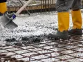 Obreros con botas amarillas trabajan con cemento fresco sobre una malla de ferralla.