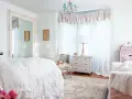 Dormitorio con cama blanca con volantes, espejo grande, cómoda antigua y un sillón. Estilo shabby chic.