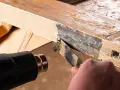 Se usa una pistola de calor para ablandar pintura vieja y descascarada de un marco de madera, facilitando su retirada con una espátula. La madera se hincha con el calor.