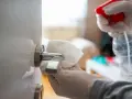 Manos enguantadas limpian un picaporte de puerta lacada en blanco con un paño.