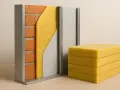 Sección de muro con ladrillos, aislamiento de fibra de vidrio y panel metálico. Bloques de fibra de vidrio apilados, demostrando sus propiedades aislantes.