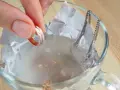 Mano sumerge anillo en agua con bicarbonato para limpiar la plata.