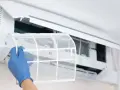 Mano con guante azul extrae filtro de aire acondicionado para limpiarlo por dentro.