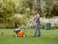 Hombre con auriculares usa un escarificador naranja para airear el césped en un jardín verde.