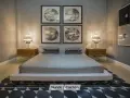 Cama moderna con cabecero tapizado, mesitas de noche de madera y lámparas de cristal. Cuadros decorativos en la pared y alfombra geométrica. Un espacio que invita a la armonía, ideal para aplicar principios de feng shui cama.