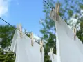 Ropa blanca desteñida de azul secándose al sol, sujeta con pinzas de madera a un tendedero.