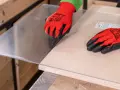 Manos con guantes rojos marcan el metacrilato sobre madera, mostrando cómo se corta el metacrilato con precisión.