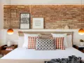 Ideas para decorar pared cabecero cama: ladrillo visto, cuadros modernos y lámparas naranjas.
