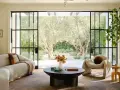 Salones modernos y elegantes con sofá curvo, sillón acogedor y mesa de centro, con vistas a un jardín de olivos.