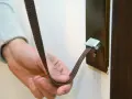 Mano sujetando una cinta marrón que se ha roto la cuerda de la persiana, enganchada a un soporte metálico.