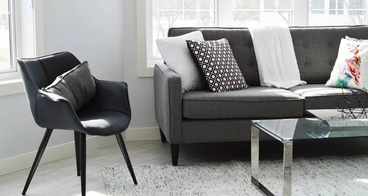 Un sillón negro y un sofá gris con cojines decorativos, listos para aprender como tapizar un sofa y renovar tu sala.