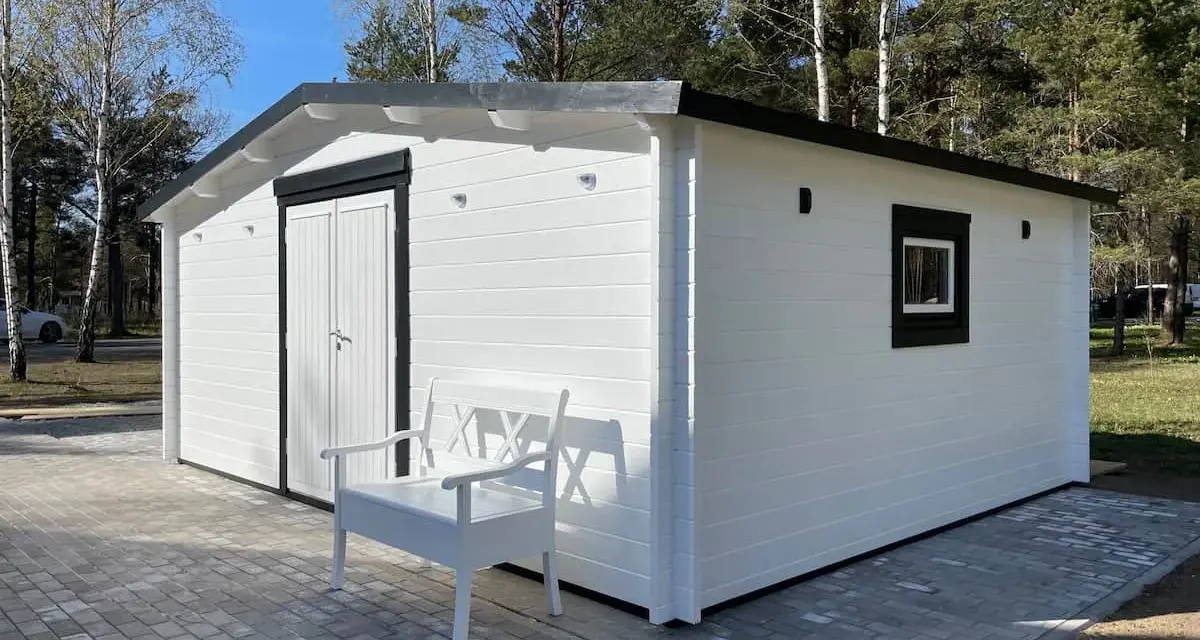 Caseta blanca con puerta doble y ventana, ideal para hacer caseta con palets. Un banco blanco invita a sentarse.