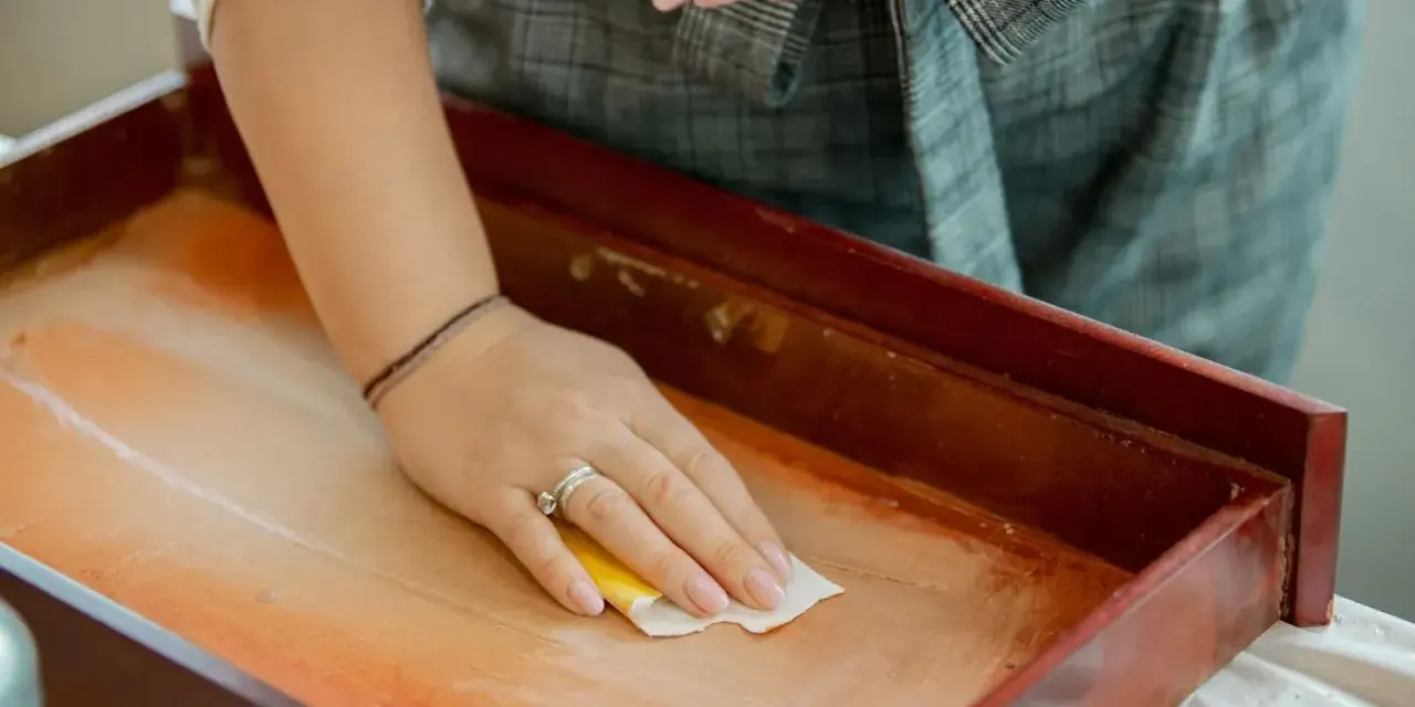 Mano limpiando un cajón de madera antiguo con un paño. Un paso esencial para saber como limpiar muebles de madera antiguos.