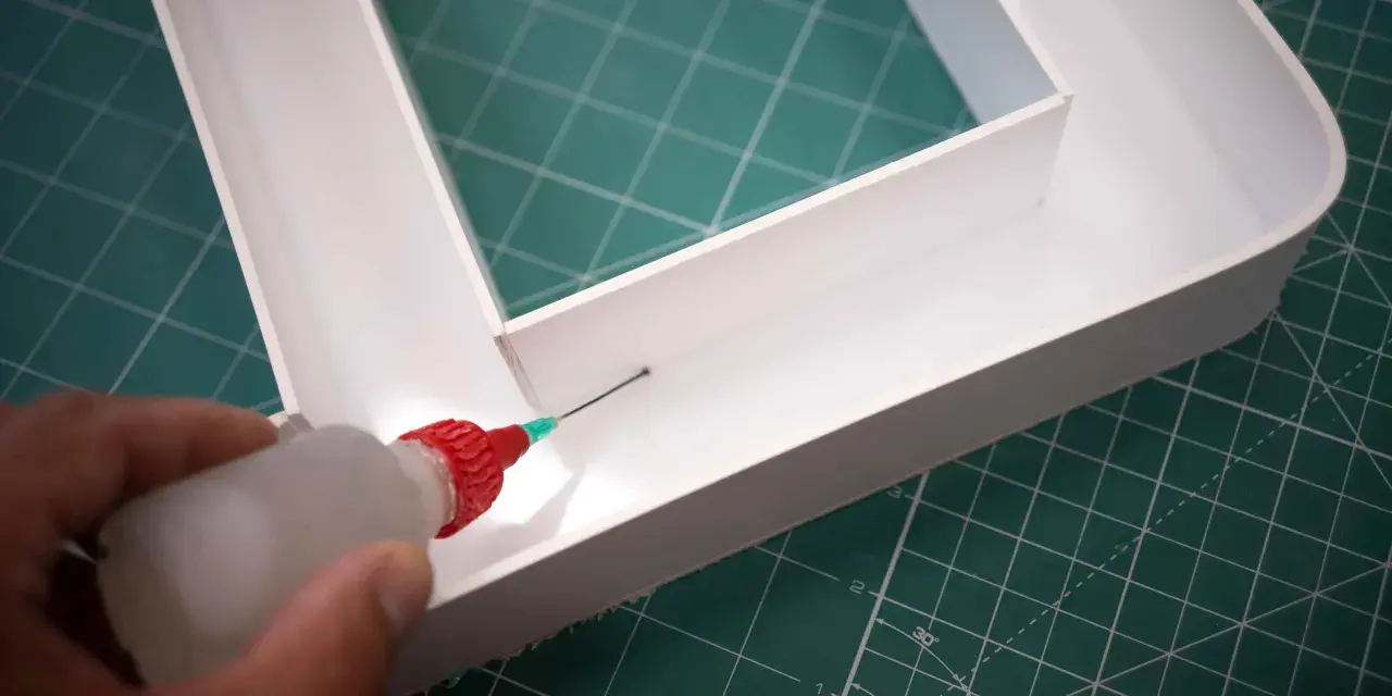 Aplicando adhesivo con precisión para saber como pegar el metacrilato y unir las piezas de forma segura.