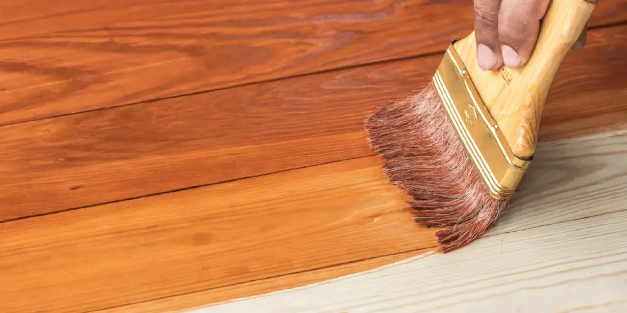 Aplicando barniz a una casa de madera para su mantenimiento. La brocha extiende el producto sobre las tablas.