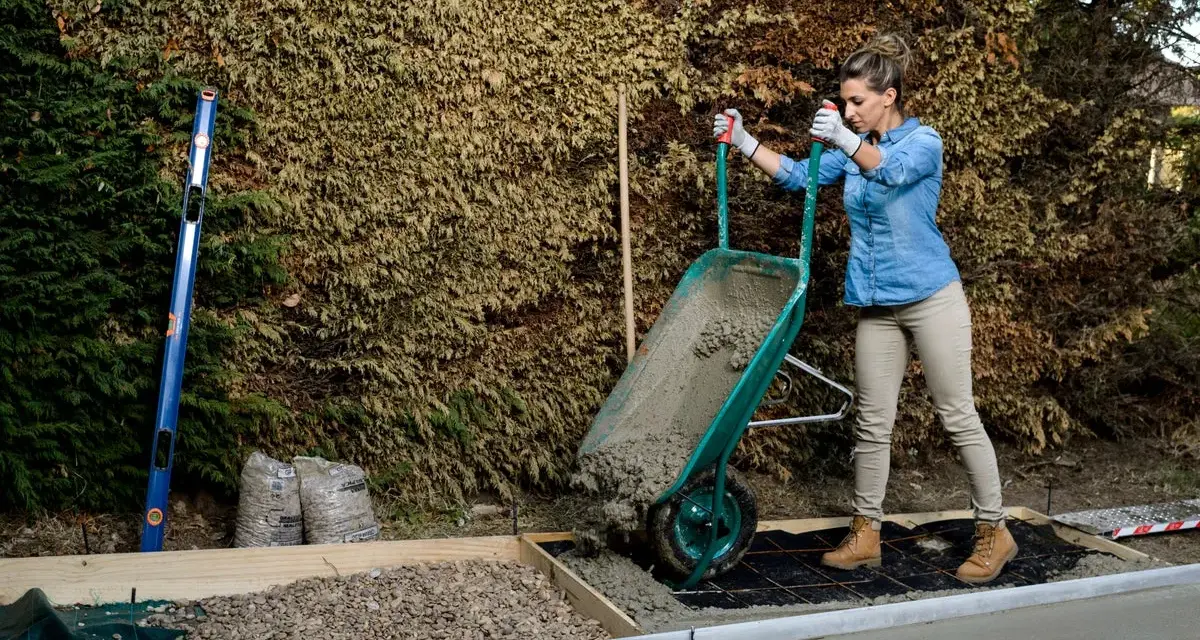 Mujer vertiendo hormigón de carretilla para como hacer una base de hormigon. Se ven herramientas y materiales de construcción.