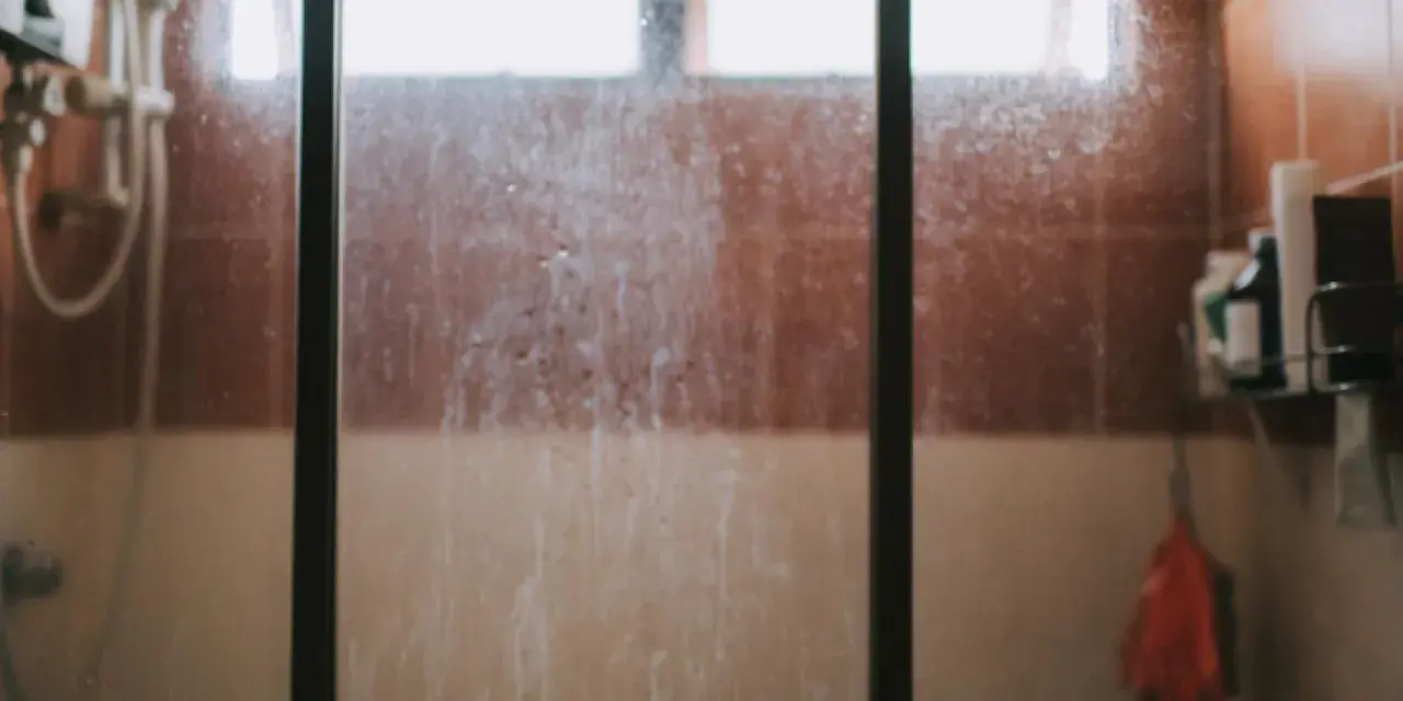 Vidrio de ducha sucio, con marcas de agua y jabón. Un recordatorio visual de cómo limpiar cristales para un baño reluciente.