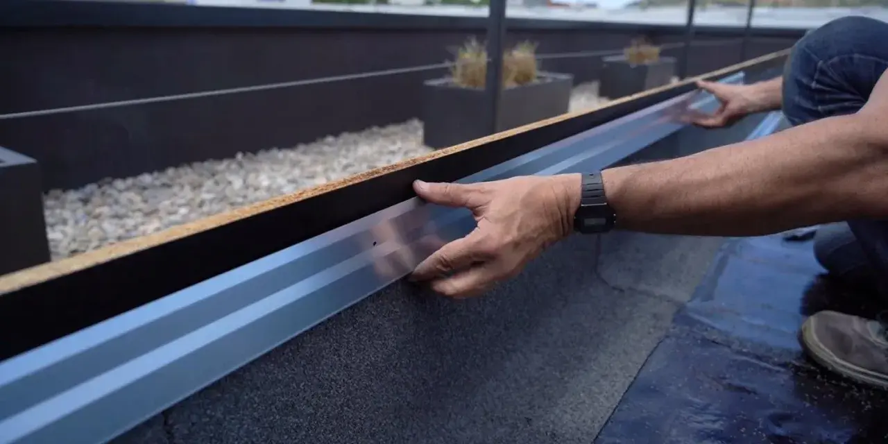 Instalación de tela asfáltica en tejado, un operario ajusta un perfil metálico.