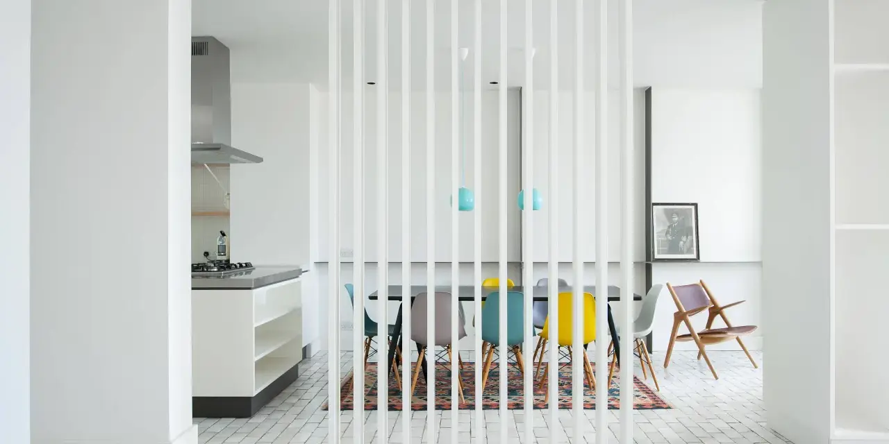 Elegante solución para dividir salón en dos ambientes con un separador de lamas blancas. Cocina moderna y comedor con sillas de colores.