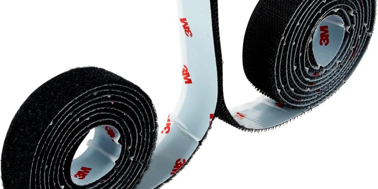 Dos rollos de cinta adhesiva negra, que es velcro, con el logo de 3M en el reverso.
