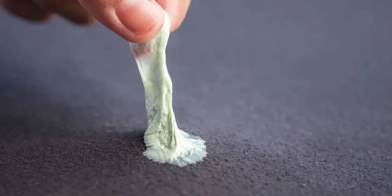 Mano retirando chicle pegado a tela. Aprende como quitar chicle de la ropa fácilmente.