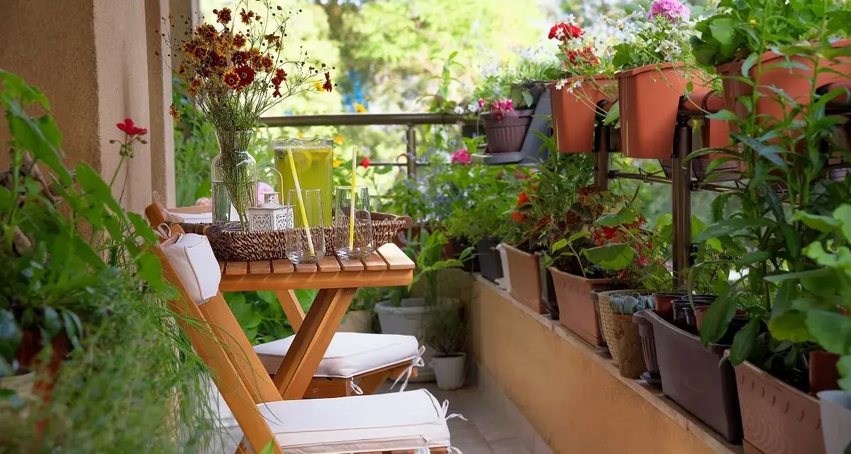 Un balcón acogedor con mesa de madera, sillas, jarra de limonada y muchas plantas. La decoración de mini balcones crea un oasis verde.
