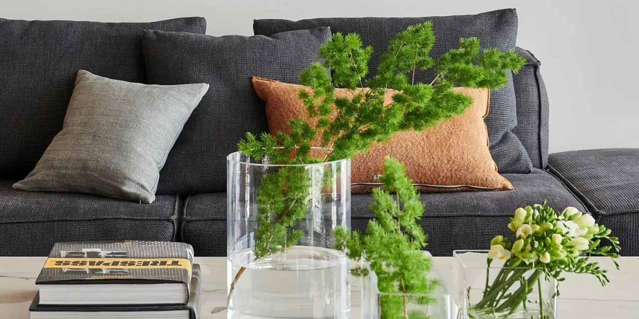 Ideas para decorar mesa de centro rectangular: jarrones con ramas verdes y flores, junto a libros apilados.