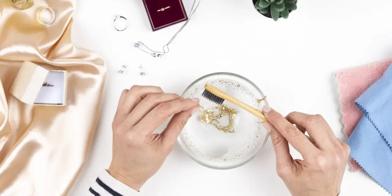 Manos limpian una cadena de oro con un cepillo en agua jabonosa. Aprende como limpiar el oro para que brille como nuevo.