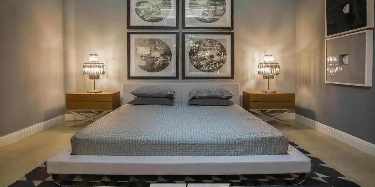 Cama moderna con cabecero tapizado, mesitas de noche de madera y lámparas de cristal. Cuadros decorativos en la pared y alfombra geométrica. Un espacio que invita a la armonía, ideal para aplicar principios de feng shui cama.