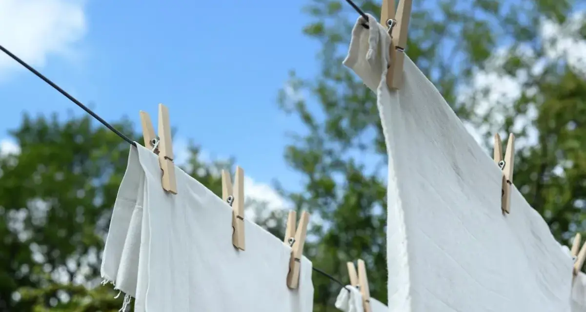 Ropa blanca desteñida de azul secándose al sol, sujeta con pinzas de madera a un tendedero.