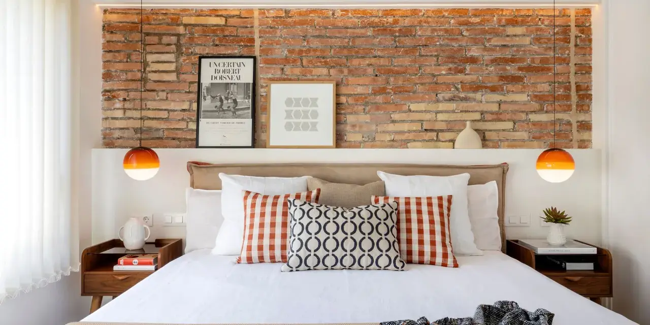 Ideas para decorar pared cabecero cama: ladrillo visto, cuadros modernos y lámparas naranjas.