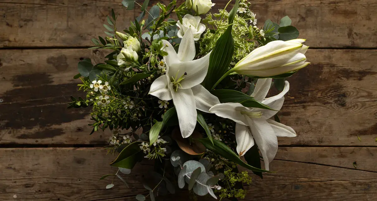 Un ramo de lirios blancos y rosas sobre madera rústica. La pregunta de cuanto dura un ramo de flores depende de su cuidado.