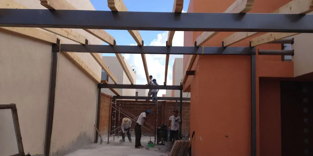 Trabajadores construyen la estructura de un garaje, instalando vigas de metal y madera.