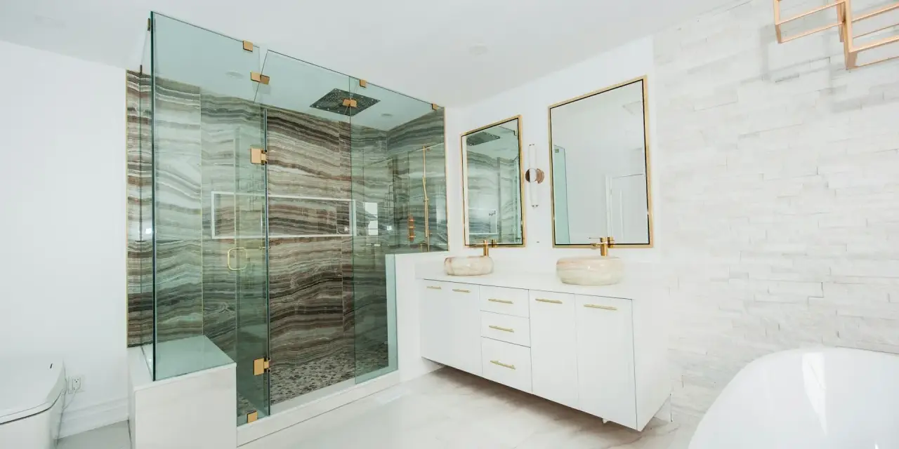 Elegante baño moderno con ducha de cristal, lavabos sobre encimera y detalles dorados. Ideas para decorar un baño de lujo.