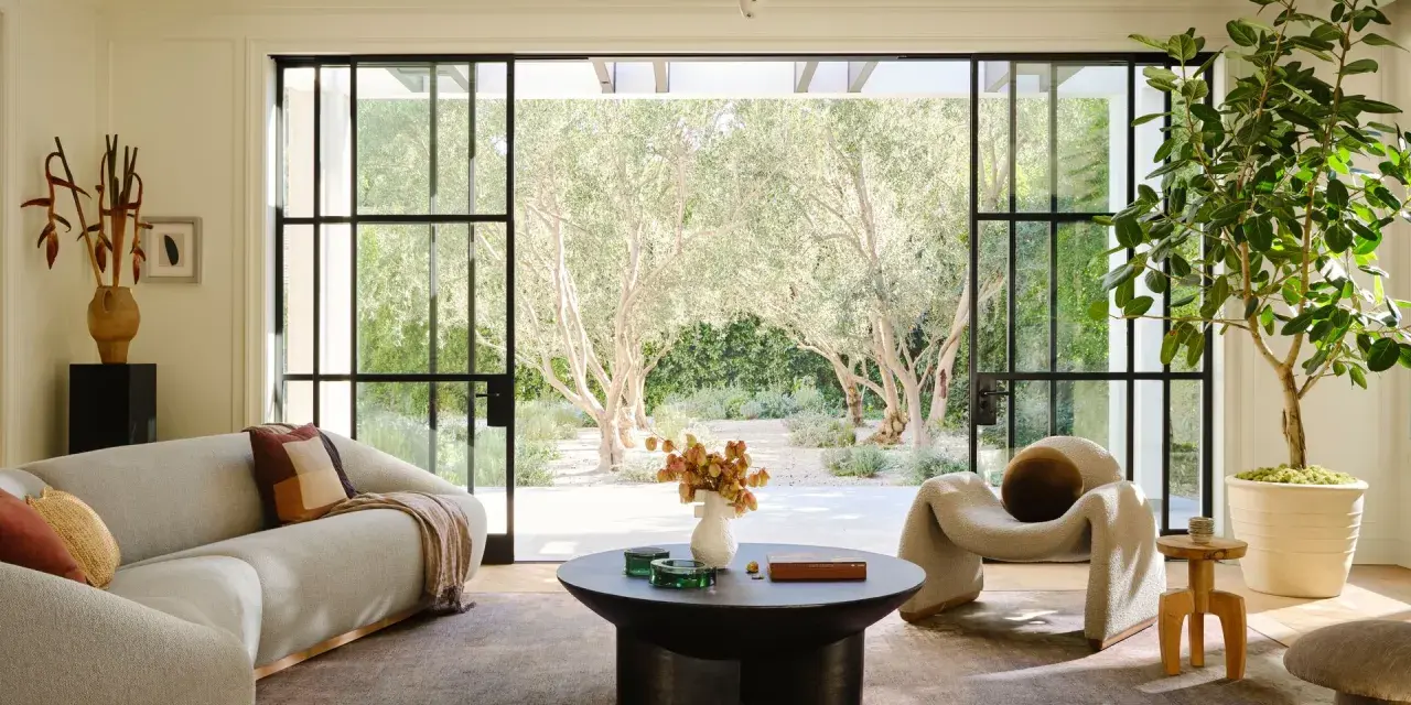 Salones modernos y elegantes con sofá curvo, sillón acogedor y mesa de centro, con vistas a un jardín de olivos.