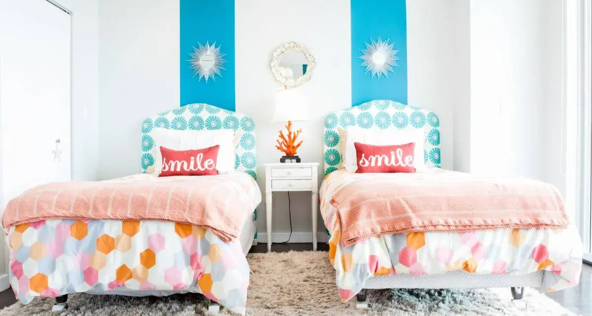 Dos camas gemelas en habitaciones pequeñas, decoradas con cojines que dicen "smile" y ropa de cama colorida.