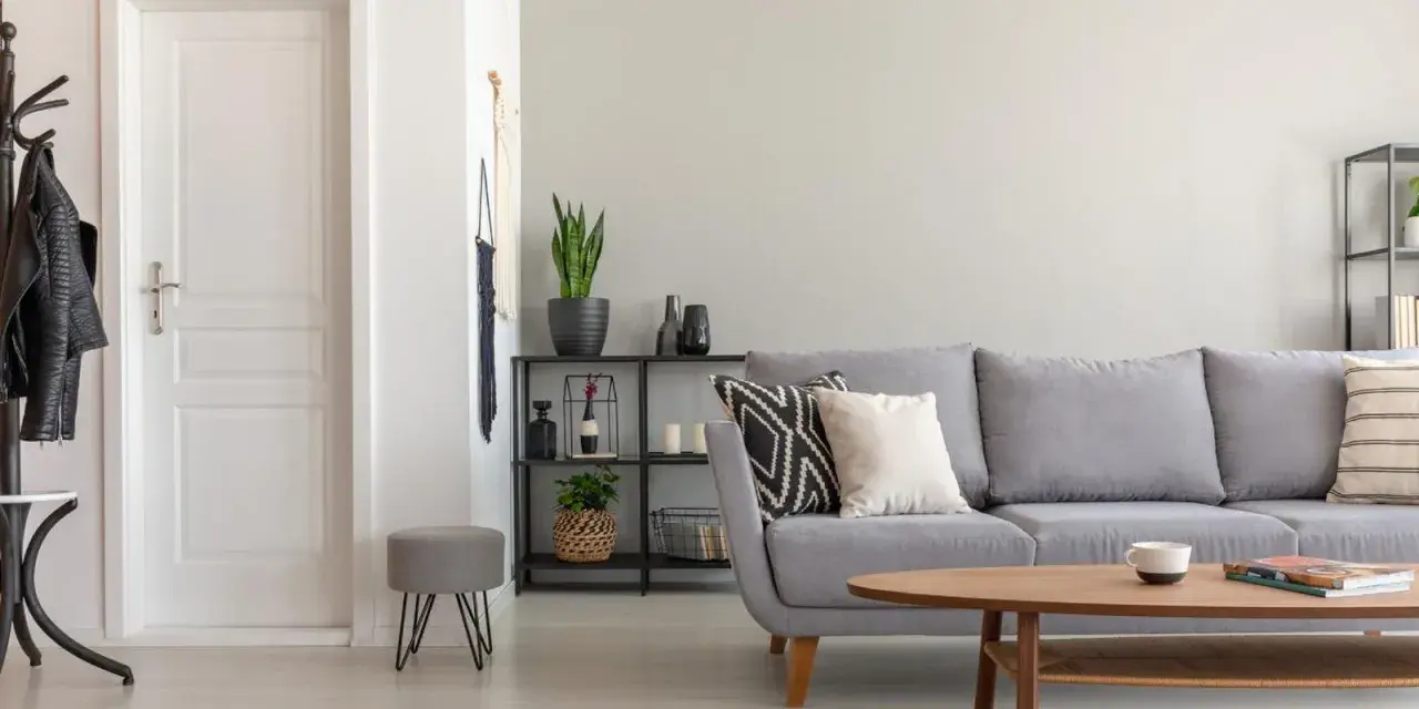 Un salón moderno con sofá gris, mesa de centro de madera y puerta blanca. El suelo claro ayuda a combinar suelo y puertas, creando un espacio luminoso.