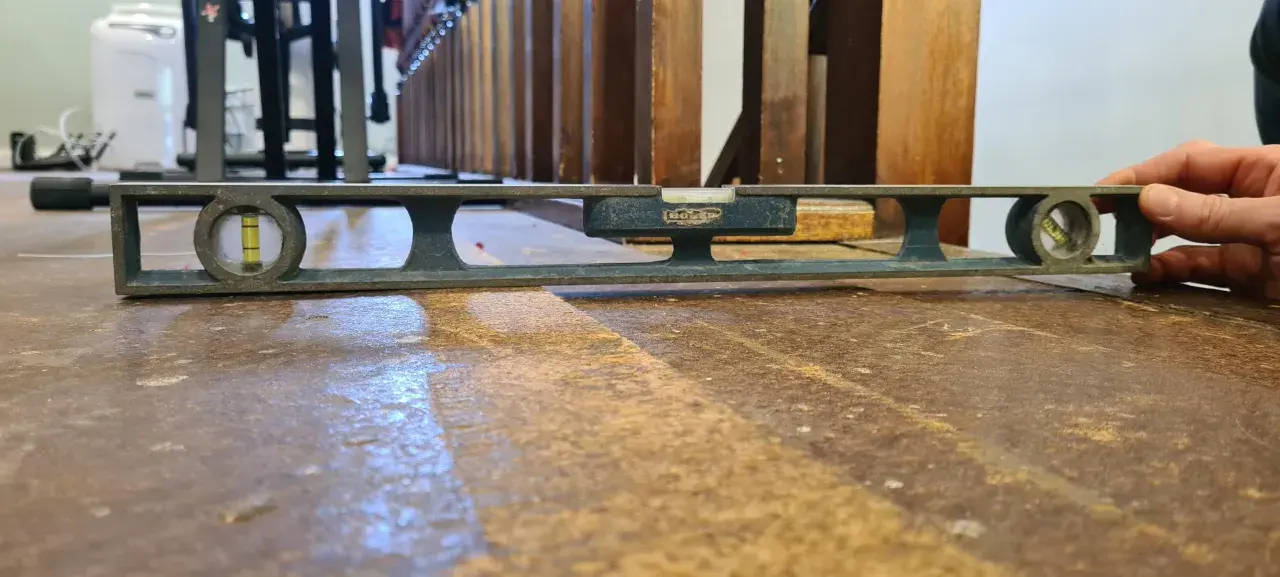 Nivelando un suelo de madera antiguo con un nivel de burbuja. La herramienta muestra que el suelo está ligeramente inclinado.