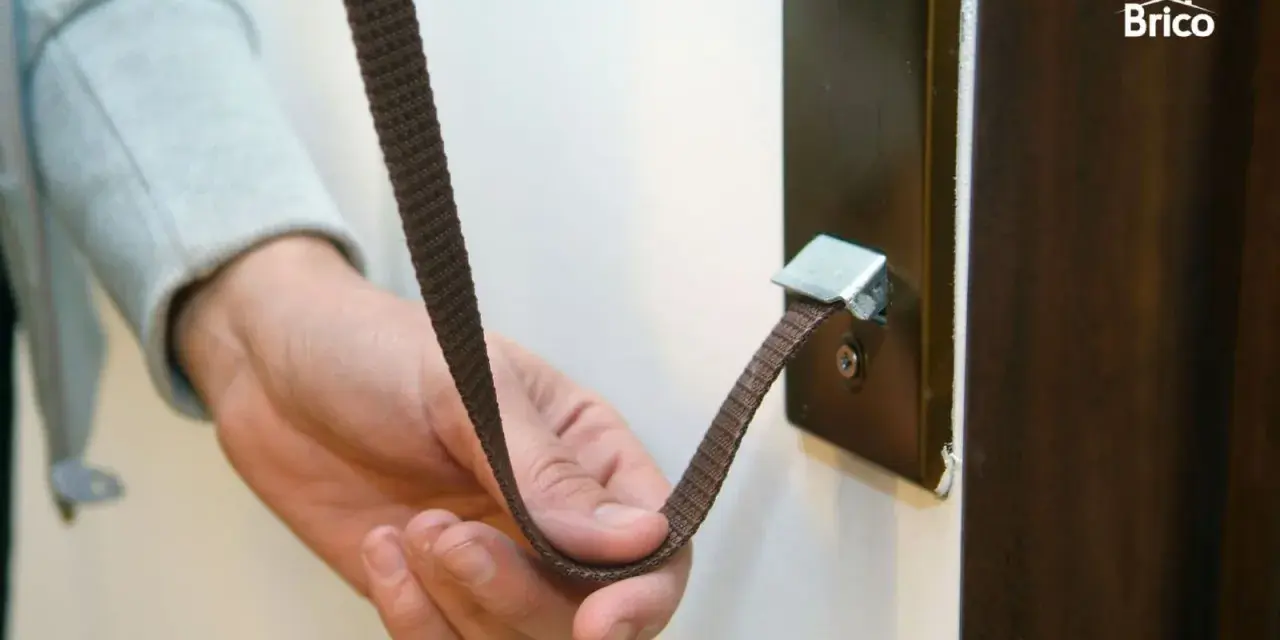 Mano sujetando una cinta marrón que se ha roto la cuerda de la persiana, enganchada a un soporte metálico.