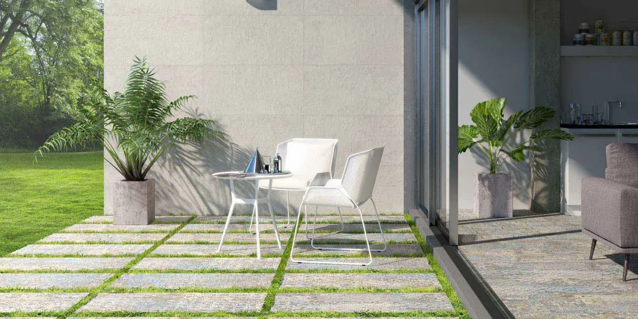 Terrazas pequeñas con encanto: un camino de baldosas y césped lleva a una mesa y sillas blancas, con plantas y un jardín verde.