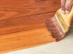 Aplicando barniz a una casa de madera para su mantenimiento. La brocha extiende el producto sobre las tablas.